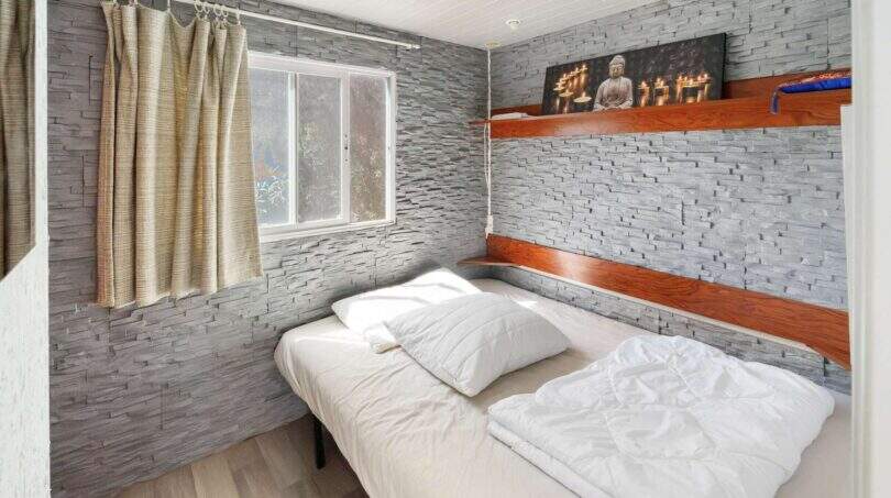 Schlafzimmer der Finca Algaida mit Steinwand, Holzregalen, Doppelbett und Buddha-Kunstwerk