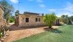 Rustikale Steinvilla der Finca Algaida mit Solarpanelen, gepflegtem Rasen und mediterranem Garten unter blauem Himmel.