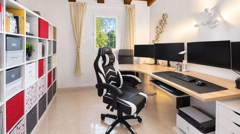 Heimarbeitszimmer der Finca Algaida mit Gaming-Stuhl, drei Monitoren, L-Schreibtisch und Regal mit Holzbalkendecke.