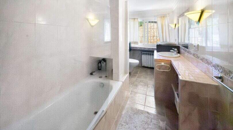 Geräumiges Badezimmer der Finca Algaida mit Badewanne, Waschtisch, Bidet und großem Spiegel mit Wandleuchten.