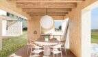 Überdachte Terrasse mit rundem Holztisch, Designerstühlen und Kugellampe, Blick auf grüne Landschaft bei Petra