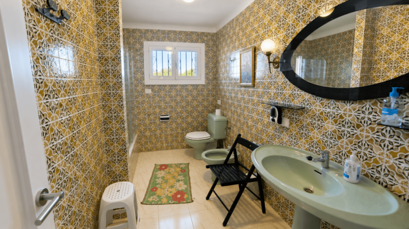Geräumiges Badezimmer der Mallorca-Villa mit grüner Sanitärausstattung und charakteristischen Mosaikfliesen in Gold-Weiß