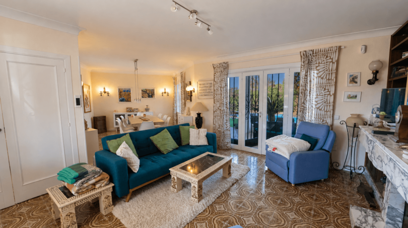 Helles Wohnzimmer der Mallorca-Villa mit blauem Sofa, Marmorkamin und Zugang zum Garten.