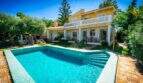 Mallorca-Villa in Llucmajor mit türkisblauem Pool, Holzterrasse, Balkon und üppigem Garten unter blauem Himmel.