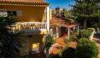 Mediterrane Villa in Llucmajor mit gelbem Fassade, Balkon, Terrakotta-Dach und üppigem Garten mit Palmen.