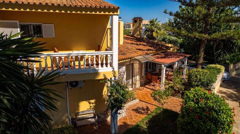 Mediterrane Villa in Llucmajor mit gelbem Fassade, Balkon, Terrakotta-Dach und üppigem Garten mit Palmen.