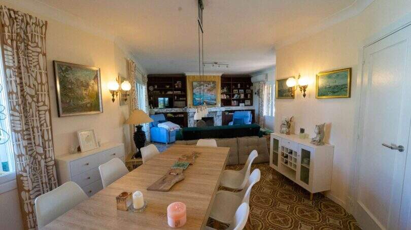 Helles Wohn-Esszimmer der Mallorca-Villa in Llucmajor mit Holztisch, Bücherregal und gemustertem Originalboden.