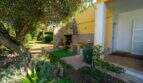 Steinbarbecue im Garten der Mallorca-Villa in Llucmajor, umgeben von üppiger mediterraner Vegetation und gelbem Hausanbau.