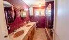Badezimmer der Mallorca-Villa in Llucmajor mit Doppelwaschbecken, Dusche und markanten roten Wandfliesen.