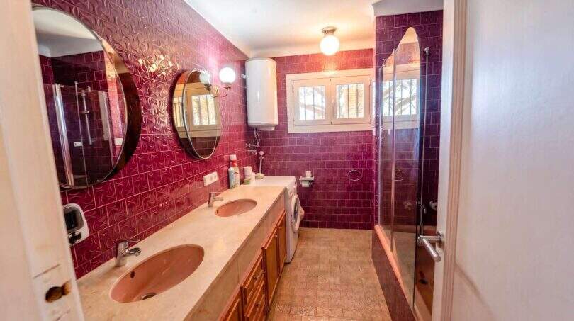 Badezimmer der Mallorca-Villa in Llucmajor mit Doppelwaschbecken, Dusche und markanten roten Wandfliesen.