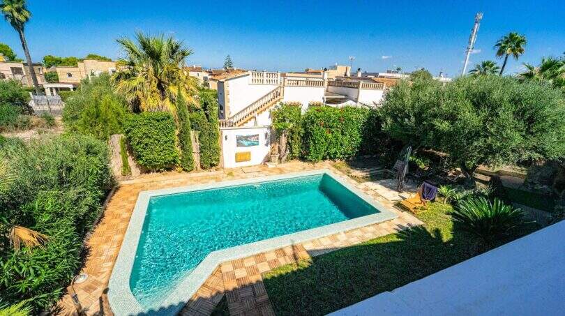Villa in Llucmajor mit türkisblauem Pool, mediterranem Garten und weißer Fassade unter blauem Himmel.