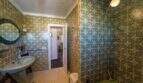 Badezimmer der Mallorca-Villa mit grün gemusterten Fliesen, rundem Spiegel und Waschbecken in Llucmajor