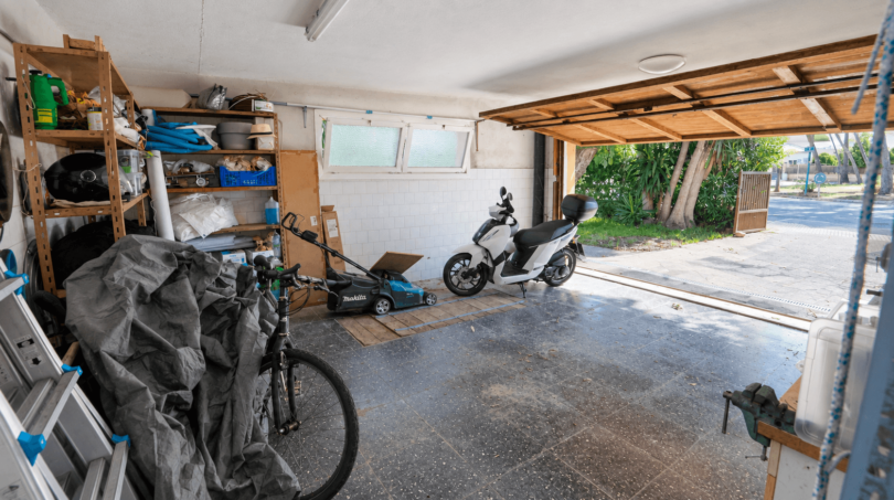 Geräumige Garage der Mallorca-Villa in Llucmajor mit Motorroller, Fahrrad, Rasenmäher und Regalen, direkter Ausgang zum Freien.