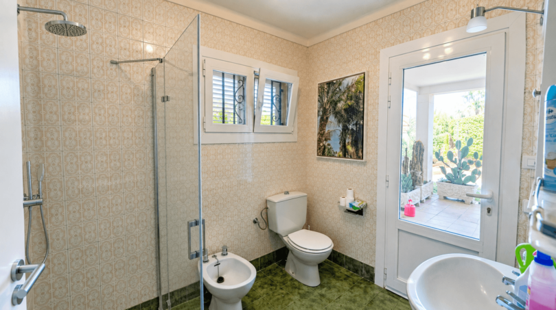 Helles Badezimmer der Mallorca-Villa mit Glasdusche, Bidet, WC und Gartenblick durch Glastür.