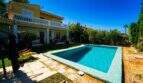 Villa in Llucmajor mit türkisblauem Pool, Holzterrasse, Garten und gelbem Haus mit Balkon.