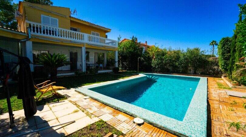 Villa in Llucmajor mit türkisblauem Pool, Holzterrasse, Garten und gelbem Haus mit Balkon.
