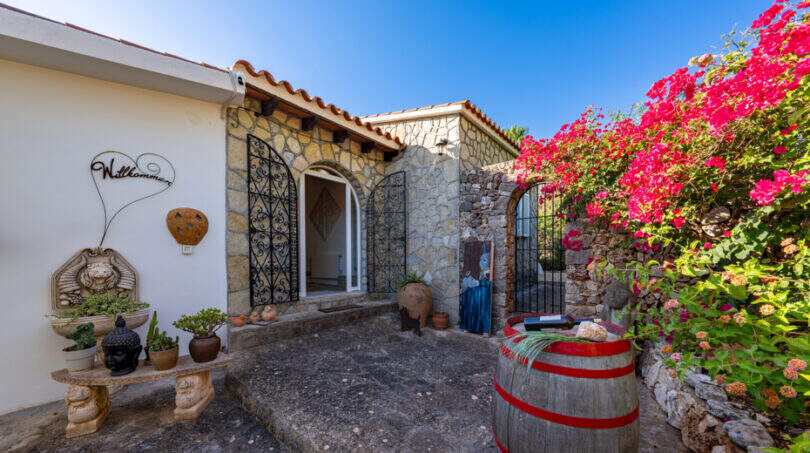 Rustic entrance area of the sea view villa in Cala Murada with stone walls, wooden barrel and bougainvillea.