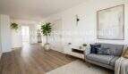 Área de estar clara del apartamento esquinero de nueva construcción en Cala Millor con suelo de madera, sofá gris y mobiliario moderno.