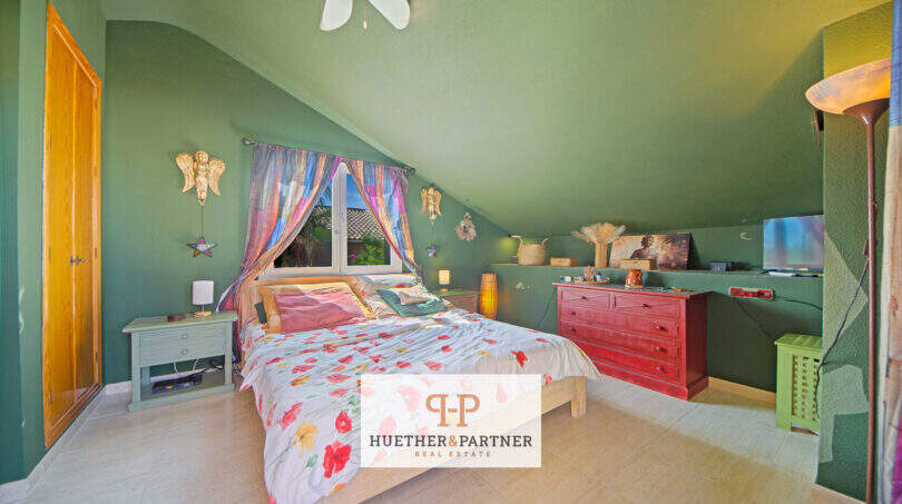 Gemütliches Schlafzimmer mit Dachschräge, grünen Wänden, Doppelbett und roter Kommode in Cala Murada.