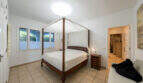 Bright bedroom of the sea view villa in Cala Murada with elegant wooden four-poster bed and tile flooring.