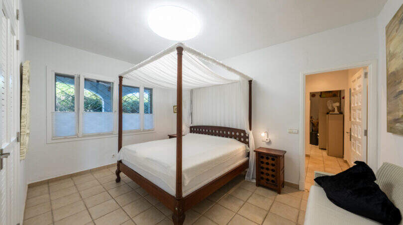 Bright bedroom of the sea view villa in Cala Murada with elegant wooden four-poster bed and tile flooring.