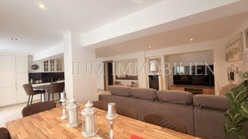 Offener Wohn-Essbereich mit Holztisch, grauem Sofa und moderner Küche in sanierter Wohnung in Pere Garau