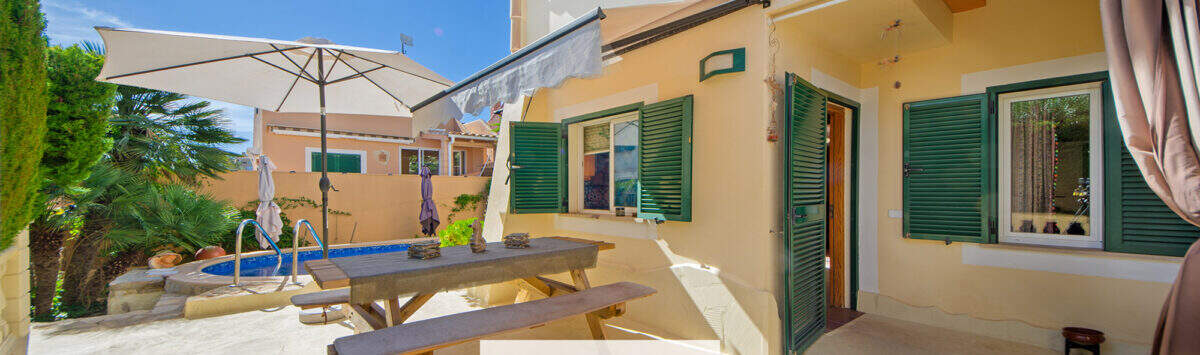Sonnige Terrasse mit Picknicktisch, Sonnenschirm und Pool eines charmanten Hauses in Cala Murada.