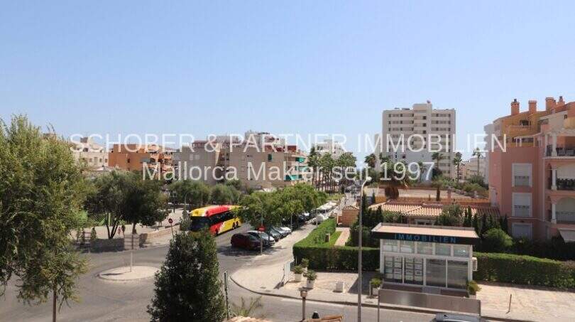 Vista de cruce de calles en Cala Millor con edificios residenciales, áreas verdes y autobús, ubicación cerca de la playa visible.
