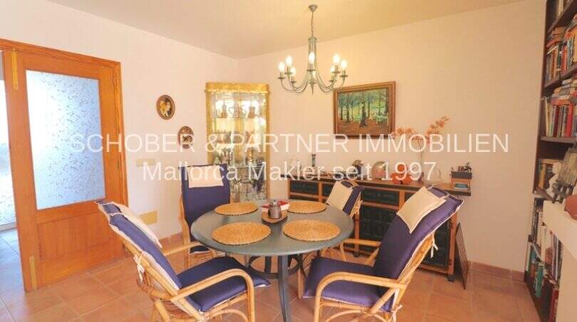 Helles Esszimmer mit rundem Tisch, Rattanstühlen, Vitrine und Bücherregal im Chalet Sa Coma