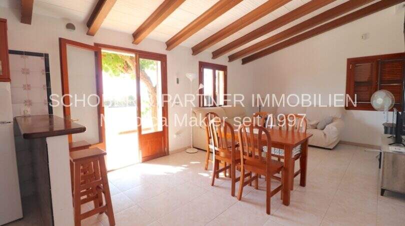 Bright living-dining room of the Mallorca finca with wooden beam ceiling, dining table and terrace access to the garden.