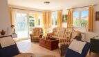 Helles Wohnzimmer mit gestreiften Sofas, goldenen Vorhängen und Terrassenzugang in einem Chalet in Sa Coma.