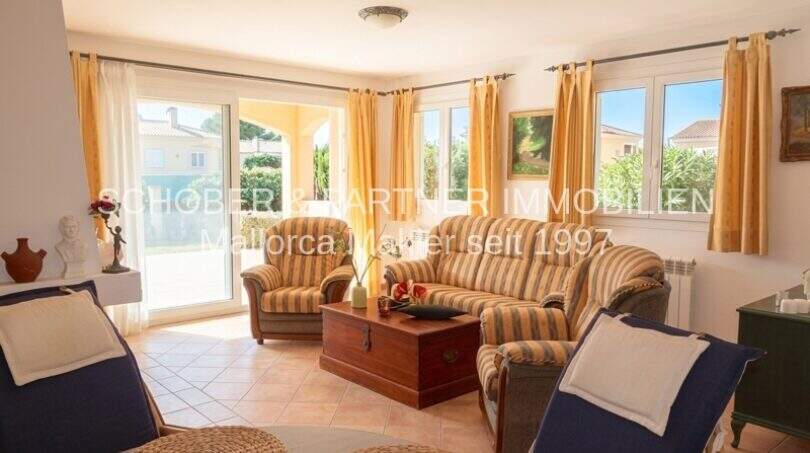 Helles Wohnzimmer mit gestreiften Sofas, goldenen Vorhängen und Terrassenzugang in einem Chalet in Sa Coma.