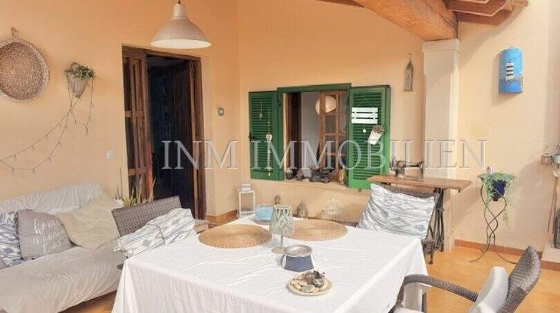 Terraza cubierta con área de comedor, techo de vigas de madera y contraventanas verdes de una casa mediterránea en Sa Ràpita
