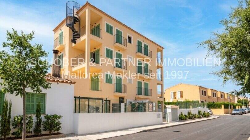 Vista exterior del apartamento esquinero de nueva construcción en Cala Millor, edificio multifamiliar amarillo con persianas verdes y balcones, escalera de caracol.