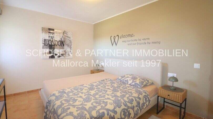 Dormitorio claro con cama doble, lema decorativo en la pared e impresión de arte de Londres en apartamento en Cala Millor