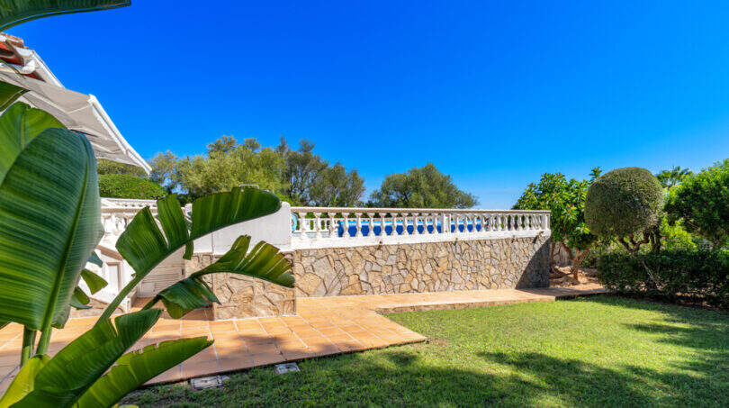 Gepflegter Garten mit Terrasse, Steinmauer, weißem Balustradenzaun und tropischer Bepflanzung der Villa in Cala Murada