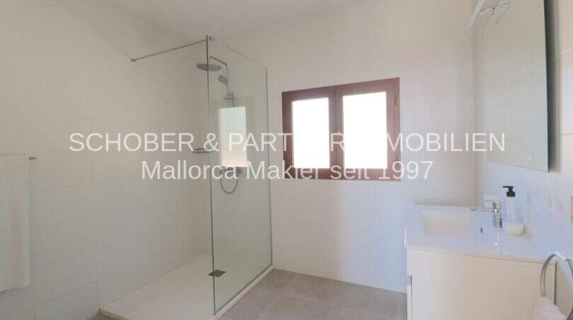 Bright bathroom of the Mallorca finca with walk-in glass shower, modern sink and small window.