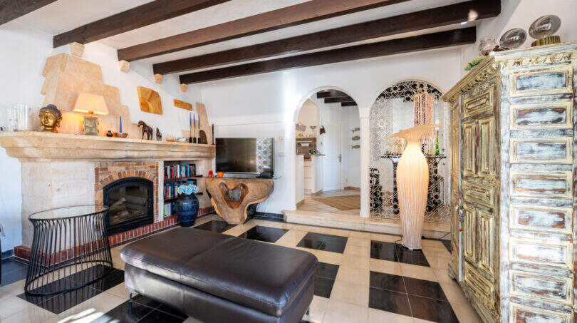 Living room of the sea view villa with fireplace, wooden beam ceiling, checkered floor and antique wooden cabinet in Cala Murada