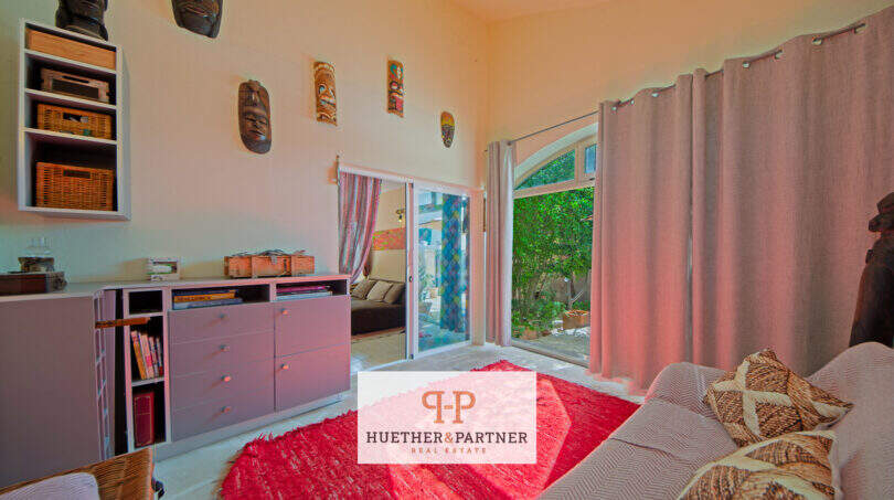 Helles Schlafzimmer mit Terrassenzugang, rotem Teppich, Holzkommode und dekorativen Masken in Cala Murada.