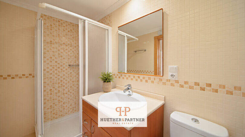 Helles Badezimmer der Erdgeschosswohnung Cala Antena mit Dusche, Waschtisch und beigen Mosaikfliesen.