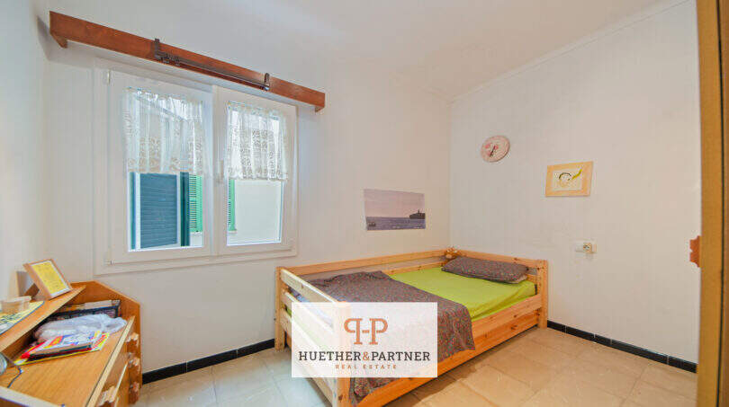 Luminoso dormitorio con cama individual, muebles de madera y ventana con vistas al mar en apartamento Porto Cristo