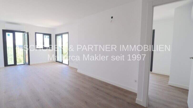 Área de estar clara del apartamento esquinero de nueva construcción en Cala Millor con suelo de madera y acceso al balcón.