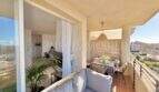 Sonniger Balkon mit Lounge-Sofa, Esstisch und Blick über Palmanova, direkt angrenzend ans helle Wohnzimmer.