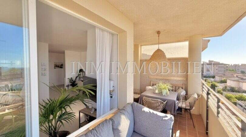 Sonniger Balkon mit Lounge-Sofa, Esstisch und Blick über Palmanova, direkt angrenzend ans helle Wohnzimmer.