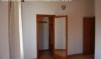 Helles Schlafzimmer der Finca Manacor mit geöffnetem Einbauschrank aus Holz und weißen Wänden.