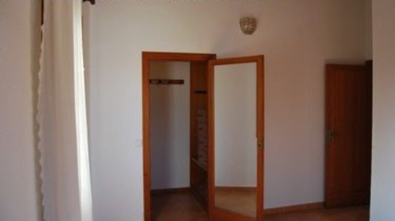 Helles Schlafzimmer der Finca Manacor mit geöffnetem Einbauschrank aus Holz und weißen Wänden.