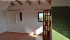 Helles Zimmer der Finca Manacor mit Terrakottaboden, Holzbalken, grünen Fliesen und Tür mit Meerblick.