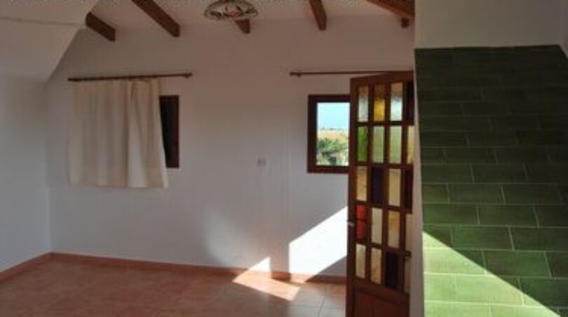 Helles Zimmer der Finca Manacor mit Terrakottaboden, Holzbalken, grünen Fliesen und Tür mit Meerblick.