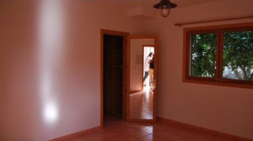 Helles Zimmer der Finca Manacor mit Terrakottaboden, Holztür und Fenster mit Gartenblick