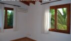 Helles Schlafzimmer der Finca Manacor mit Holzfenstern, Klimaanlage und Blick auf tropischen Garten mit Palmen.